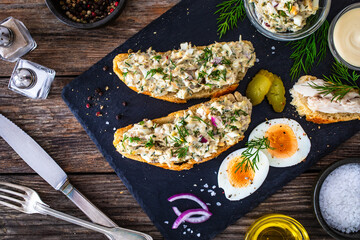 Tasty sandwich with egg salad and smoked mackerel on wooden table

