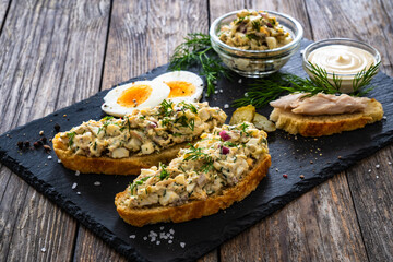 Tasty sandwich with egg salad and smoked mackerel on wooden table
