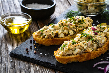 Tasty sandwich with egg salad and smoked mackerel on wooden table
