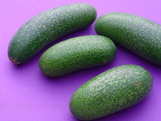 Four cocktail avocados or mini avocados on a purple background. Cocktail avocados are very small, oblong-shaped fruits that do not contain the characteristic central seed.