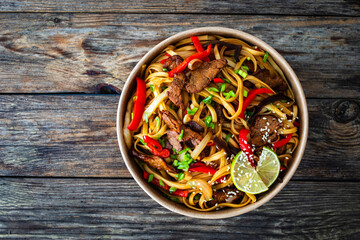 Asian style stir fried vegetables, roast beef and chow mein noodles  to go  in food box on wooden...