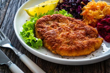 Crispy breaded fried pork chop with grated beetroots, red cabbage and sauerkraut on wooden table
