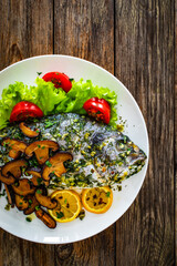 Baked sea bream, mushrooms and fresh vegetables on wooden table
