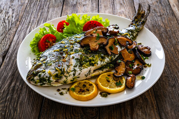 Baked sea bream, mushrooms and fresh vegetables on wooden table
