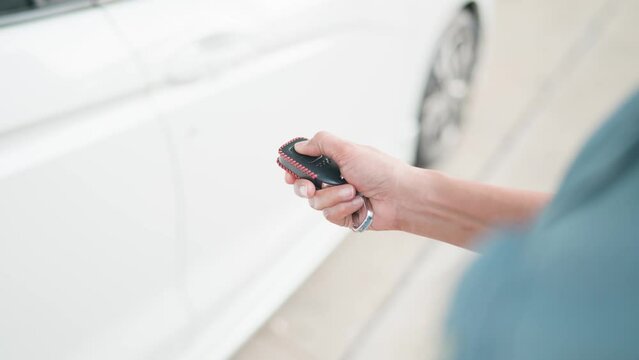 Woman opens a car door with a remote control key. A woman's hand presses on a car alarm system on the background of a parked car. Turning off the car alarm