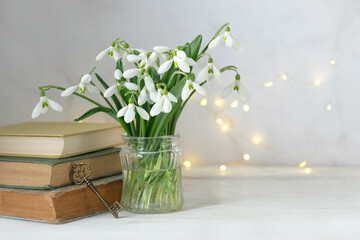 bouquet of snowdrop flowers, vintage key and books on table, abstract light background. Romantic composition with Blossoming snowdrops, symbol of spring season. Relaxation, reading time