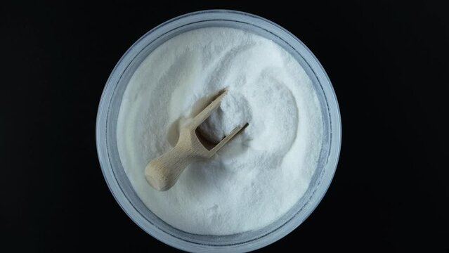 Sodium erythorbate or Sodium isoascorbate powder in disposable  plastic box with wooden spoon. Food additive E316 used predominantly in meats, poultry and soft drinks. 4K video, rotating.
