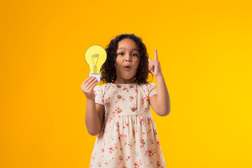Surprised child girl holding paper bulb and pointinting finger up. Success, motivation, winner, genius, idea concept