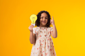 Child girl holding paper bulb and pointing finger up. Success, motivation, winner, genius, idea...