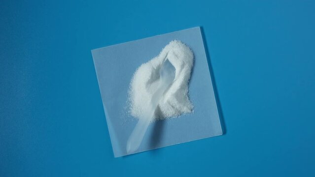 Sample of Food additive E316 on blue background. Sodium erythorbate, Sodium D-isoascorbate or araboascorbic acid. Chemical formula C6H7NaO6. White crystalline powder. 4K video, rotating.