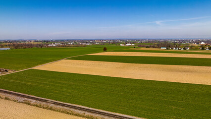 Fototapeta premium Vast Agricultural Fields With Distinctive Green And Beige Patterns Bordering A Small Town Under The Expansive Blue Sky.
