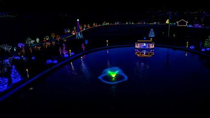 Aerial Nighttime Image Of A Pond With A Fountain And Surrounding Colorfully Lit Christmas Trees And...