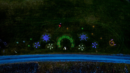 Aerial View Of A Dark Field With Colorful Light Displays In The Shapes Of Snowflakes, Wreaths, And...