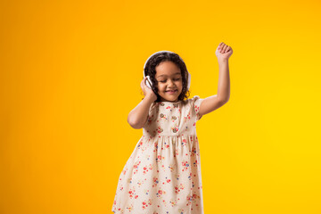 Smiling kid girl with headphones enjoying music and dancing on yellow background. Lifestyle and...