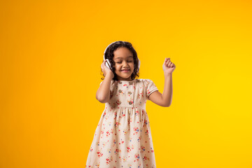 Smiling kid girl with headphones enjoying music and dancing on yellow background. Lifestyle and leasure concept