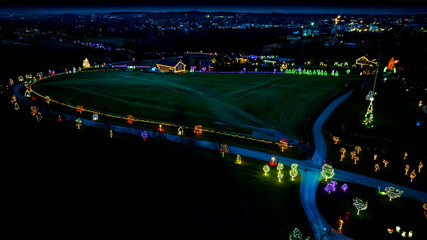 Aerial Night View Of A Winding Road Adorned With Luminous Christmas Trees Leading To A Centrally Lit Large Tree And Buildings.
