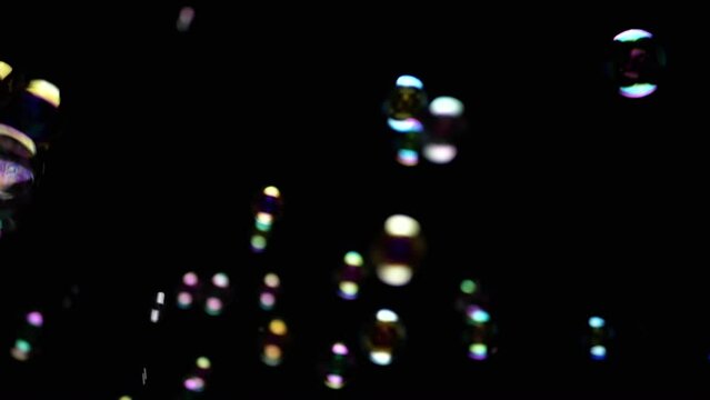 Colorful Soap Bubbles Fly in Empty Space on Isolated Black Background. Colorful lights. Many rainbow transparent bubbles randomly rotate, float, fall, burst. Blurred motion. Selective focus. Abstract.