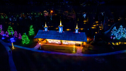 Overhead Night View Of A Building With Illuminated Rooflines And Steeples Surrounded By Trees...