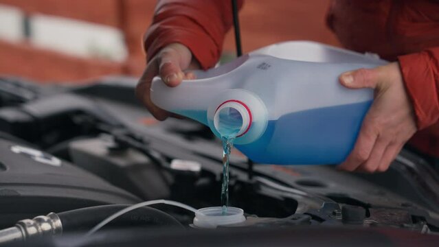Pouring winter washer fluid into car reservoir during winter, protecting it from freezing.