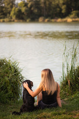 a black labrador retriever type mixed breed dog sitting hugging in the grass with a young woman on...