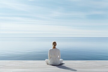 Woman meditating on the dock is looking out at the ocean - obrazy, fototapety, plakaty