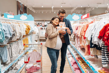 Attractive middle age couple enjoying in buying clothes and appliances for their new baby. Heterosexual couple in baby shop or store. Expecting baby concept.
