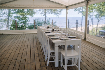 Jurmala, Latvia - july 25, 2023 - Outdoor dining setup under a tent on a wooden deck with a long...