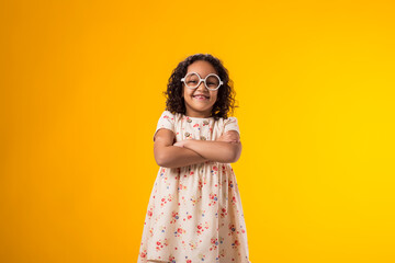 Smiling kid girl with glasses looking at camera over yellow background. Childhood and knowledge...