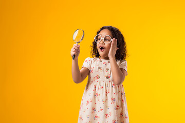 Surprised kid girl holding magnifier in hand. Education and curiosity concept