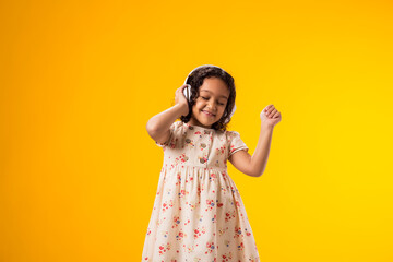 Smiling kid girl with headphones enjoying music and dancing on yellow background. Lifestyle and...