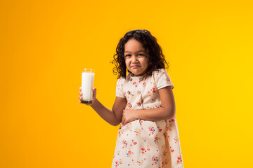 Kid girl holding glass of milk and feeling abdominal pain on yellow background. Lactose intolerance concept