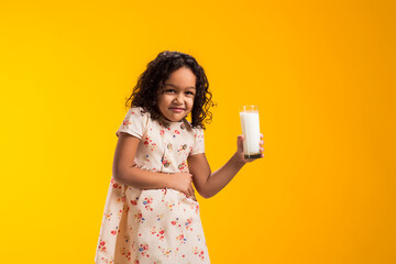 Kid girl holding glass of milk and feeling abdominal pain on yellow background. Lactose intolerance...