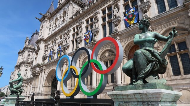 JO de Paris 2024, anneaux olympiques, c&eacute;l&egrave;bre logo symbole des jeux olympiques, devant la fa&ccedil;ade de la mairie / h&ocirc;tel de ville de Paris, avec une statue &ndash; mai 2023 (France)