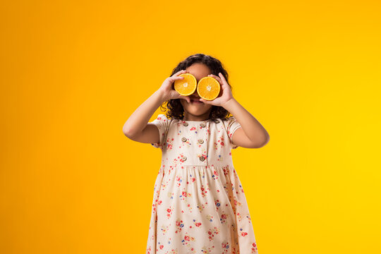 Smiling kid girl holding half of oranges near the eyes. Healthy food, vitamins and children nutrition concept