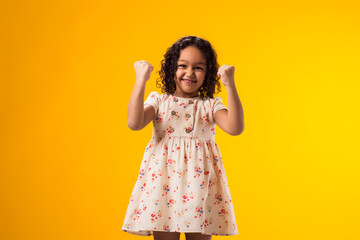 Kid girl showing winner gesture over yellow background. Success and victory concept