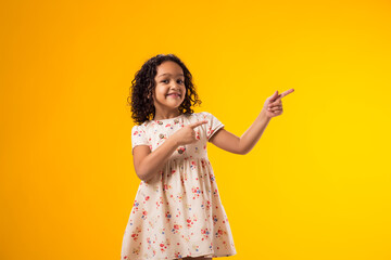 Smiling child girl pointing to an empty place on yellow background. Advertisement concept