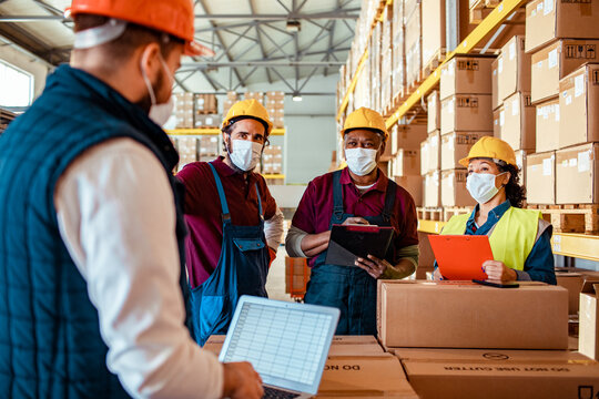 Warehouse workers in safety gear discussing logistics with laptop