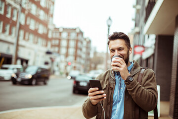 Man drinking coffee and looking at smartphone on city street