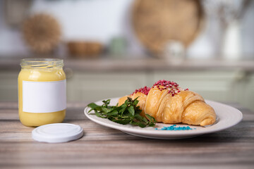 a delicious fresh croissant on a plate sprinkled with sweets and a jar of butter for spreading