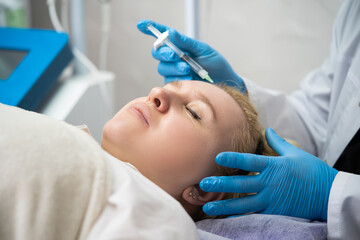 beautician man makes an injection with a cosmetic syringe in the girl's face