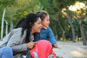 Dominican mother and son looking at a side on a balance bike in a park. Latin family.