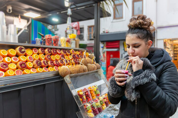 Young woman drinking healthy detox juice with straw. Female tourist enjoying takeaway  freshly squeezed juice on the street. Healthy lifestyle concept - obrazy, fototapety, plakaty