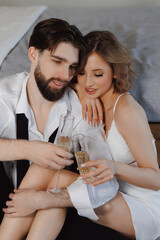 Joyful newlywed couple woman and man toasting with champagne in bed of hotel