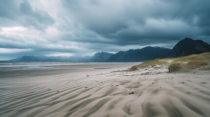 Fototapeta na wymiar Moody Landscape: Textured Beach, Calm Waters, and Majestic Mountains
