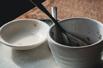 Empty dessert ceramic dishes on a white plate with a silver spoon, served on the wooden table, close-up shot.