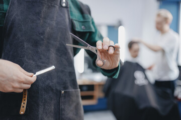 Closeup hands of hairdresser holds scissors and razor on background barbershop