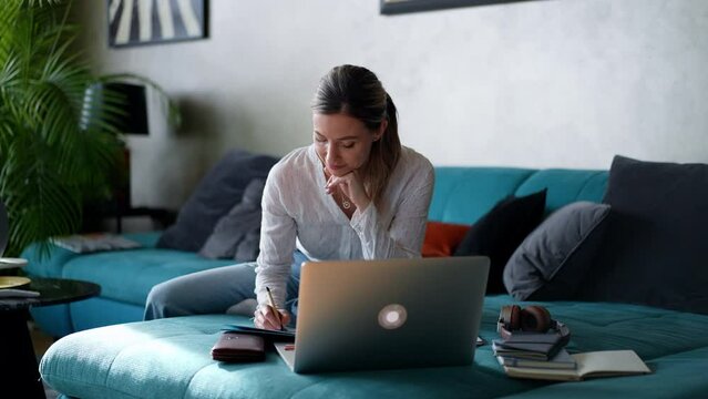 Woman paying bills online, sitting in living room, working on notebook. Online banking, internetbanking at home throught website, app.