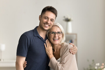 Positive handsome son man and happy blonde mature mother hugging at home with love, looking at...