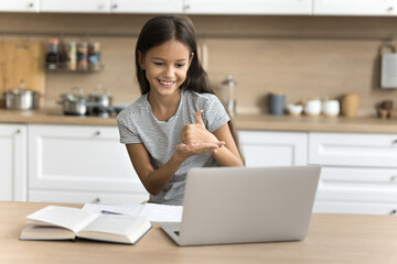 Positive pre teen schoolkid girl with hearing disability using laptop at home, studying online, talking on video conference call, using deaf language, showing hand signs at screen