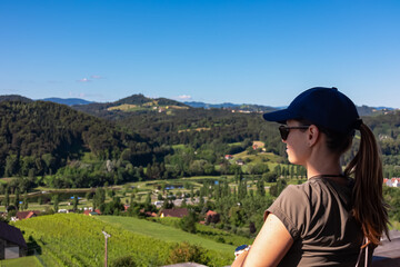 Tourist woman with scenic view from Weinleiten water tower in Ehrenhausen an der Weinstrasse, Leibnitz, South Styria, Austria. Wine plantations and vineyards over lush green hills. Styrian Tuscany